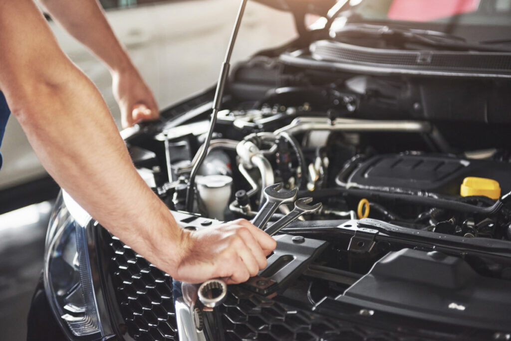 Mechaniker mit Schraubenschlüssel in der Hand beugt sich über geöffnete Motorhaube